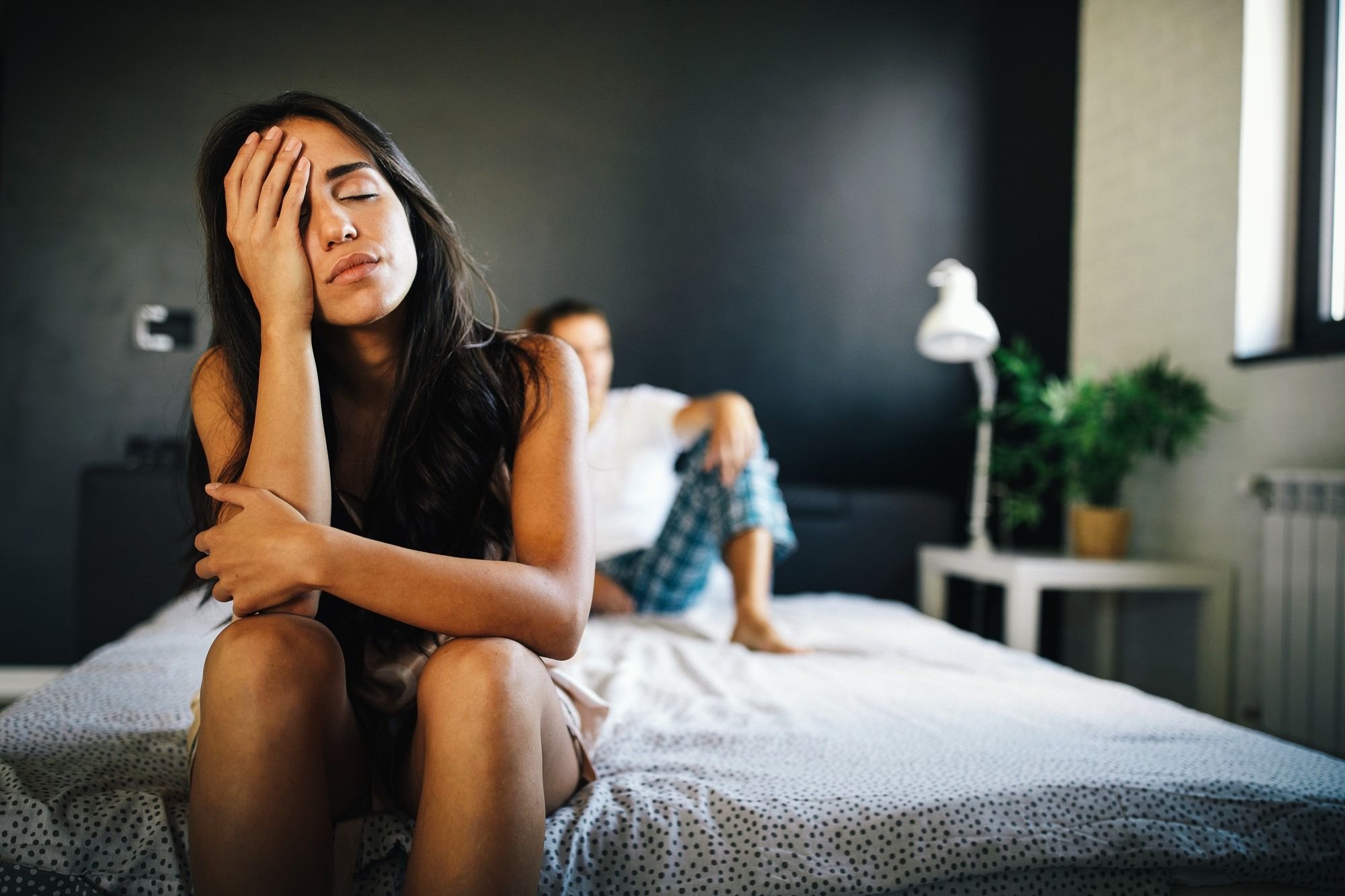 Woman sitting in bed with a face in her head, thinking. with a guy in the background blurred