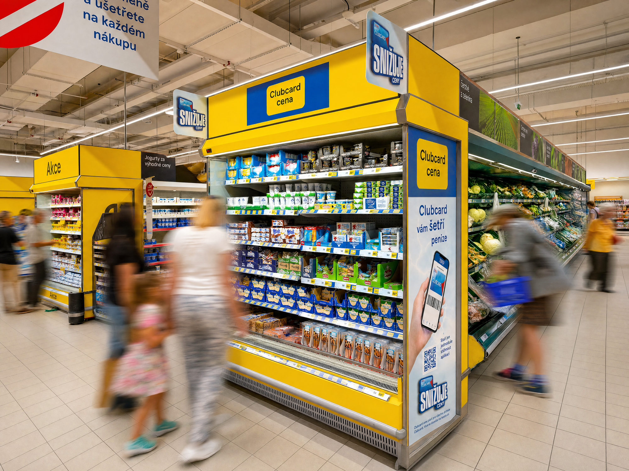 A chilled aisle end in Clubcard yellow and blue, shoppers passing in motion blur, SNIŽUJE CENY signs on every gondola head.