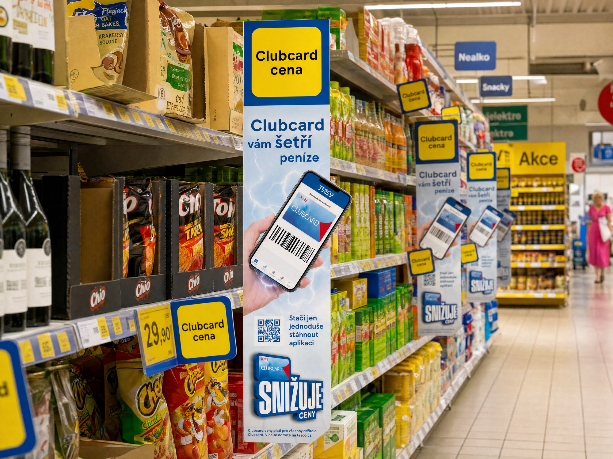 Aisle fins running the length of a Czech store, each carrying Clubcard vám šetří peníze, a phone showing the card, and the SNIŽUJE CENY lockup.