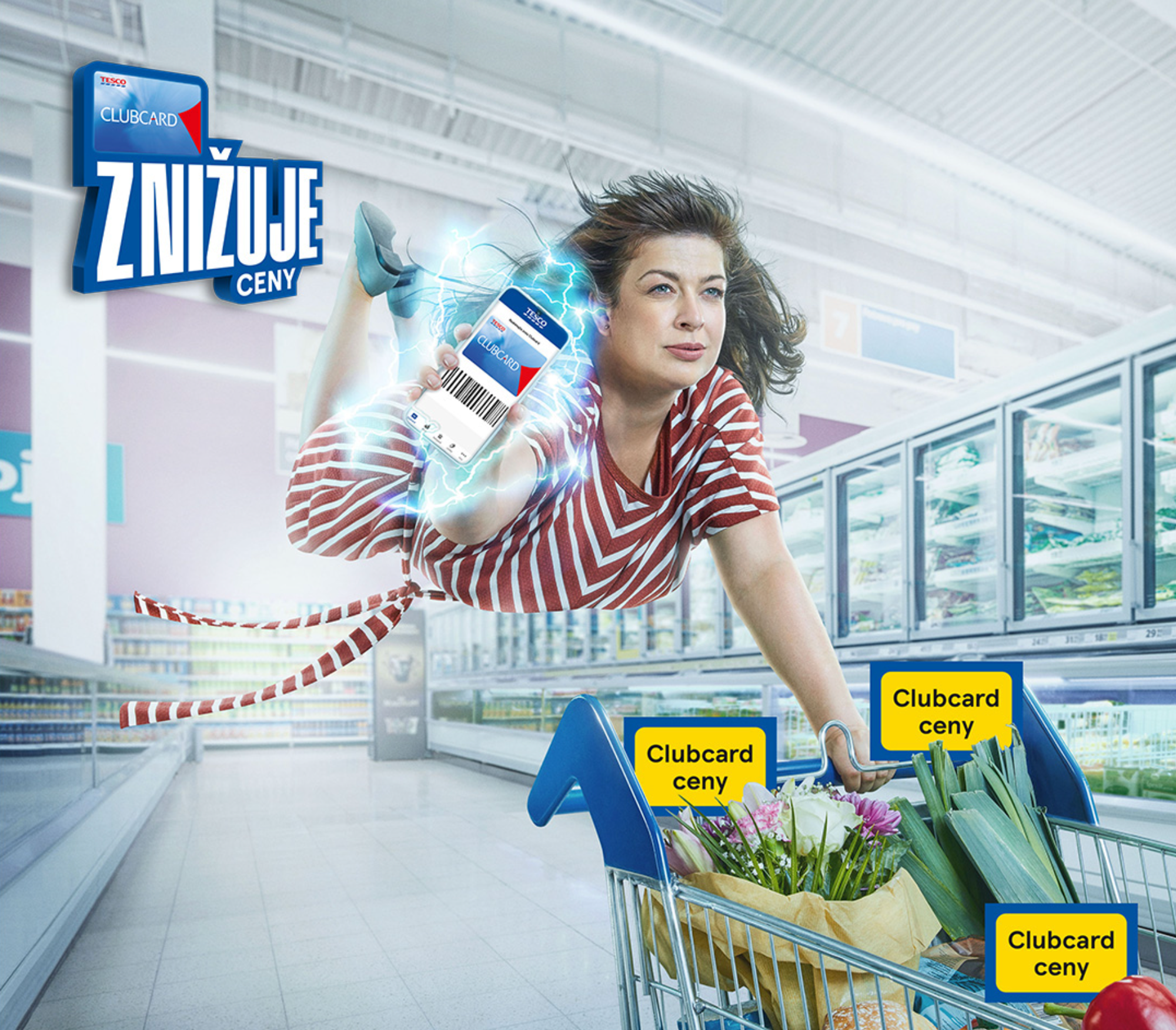 The campaign key visual — a shopper flying horizontally down a chilled aisle, holding out a phone with her Clubcard as lightning arcs from the screen. ZNIŽUJE CENY locked up top left.
