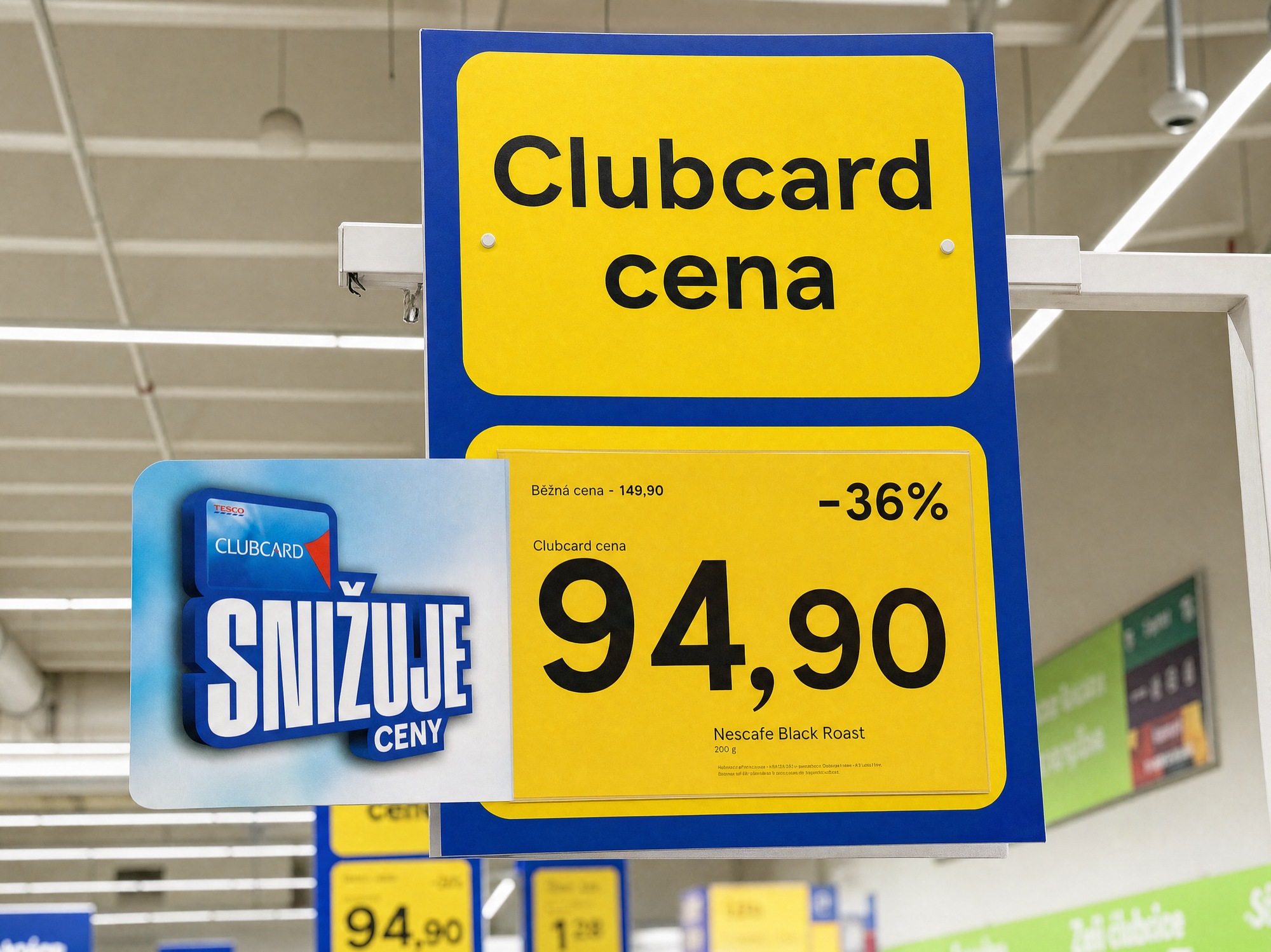 An in-store hanging sign: a yellow Clubcard cena panel carrying the price of a Nescafé jar, the SNIŽUJE CENY lockup clipped to its edge.