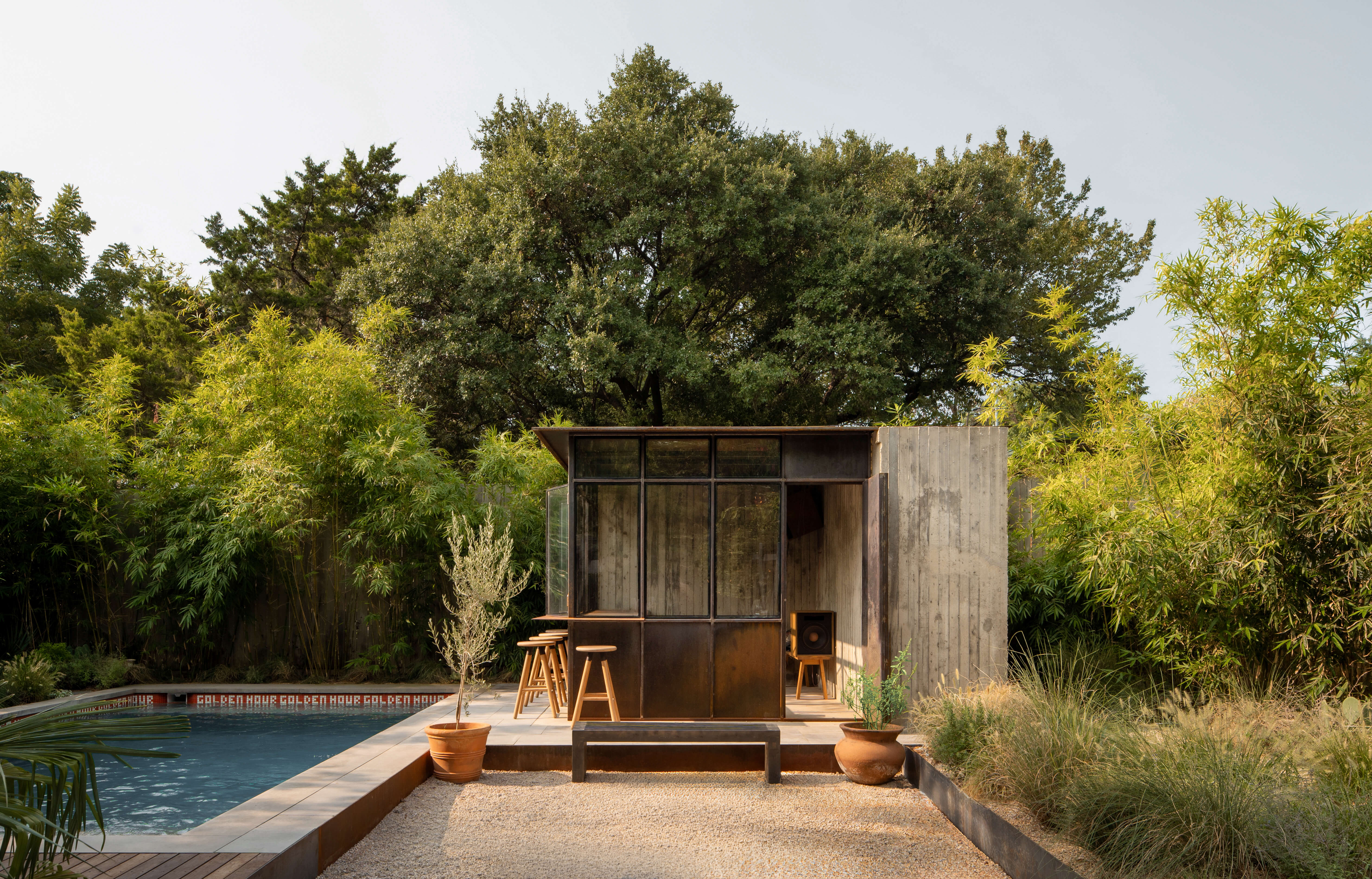 Dallas pool house tucked beneath oak trees with gravel patio and pool view