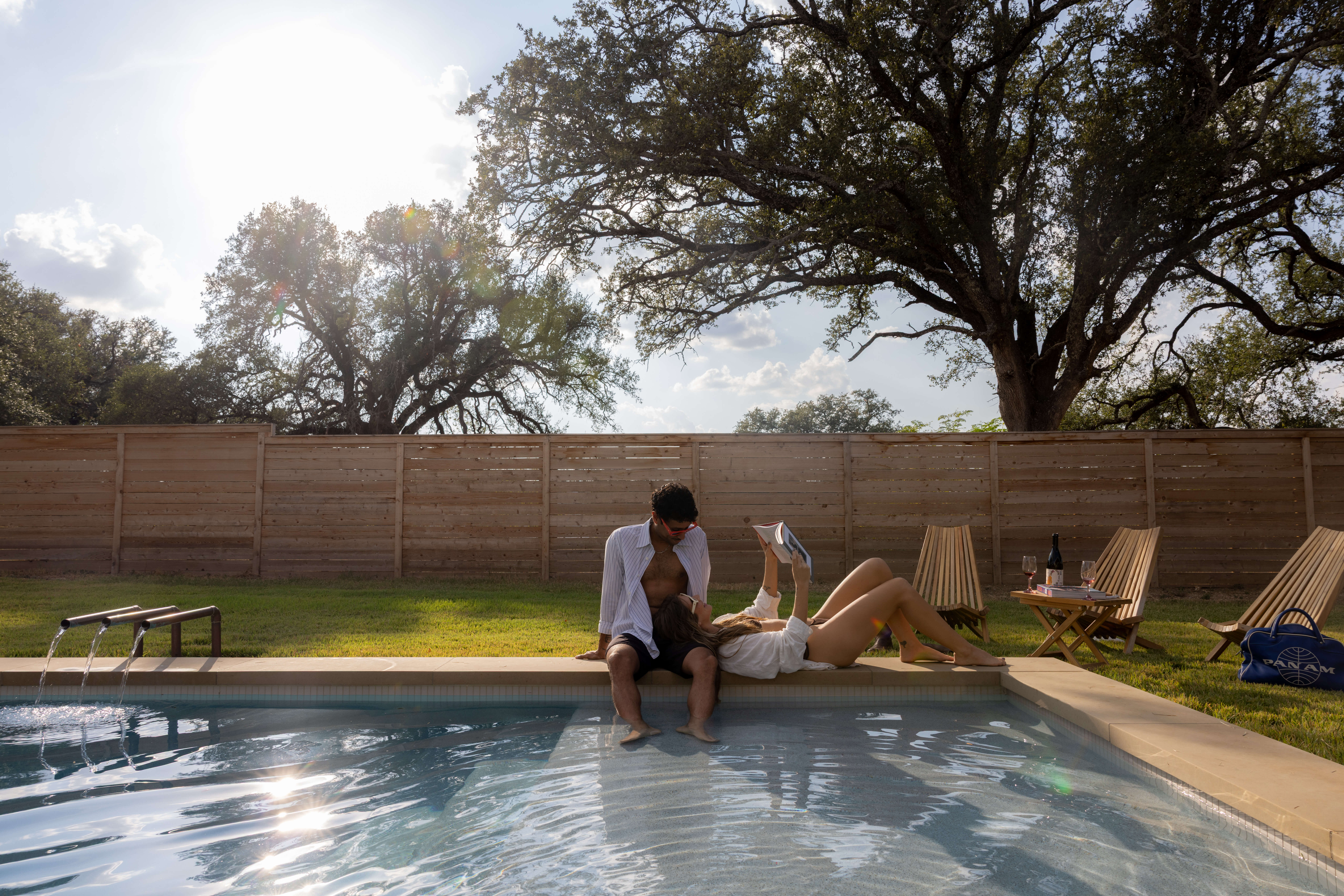 Grand Pool in Waco, featuring couple relaxing poolside with heritage oaks and horizontal wood fence