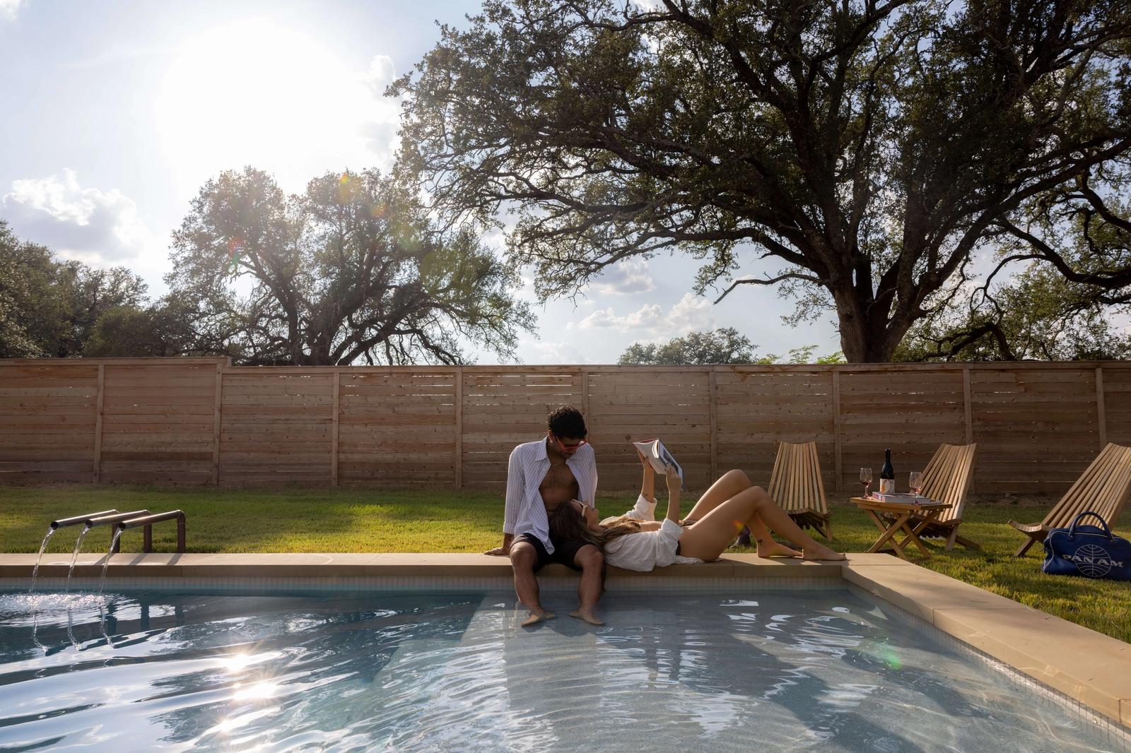 Grand Pool in Waco, featuring couple relaxing poolside with heritage oaks and horizontal wood fence