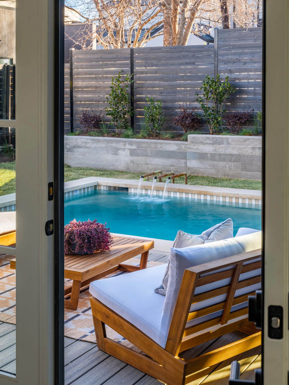 Golden Hour Pools Classic in Austin, featuring indoor-outdoor view through French doors to pool with fountain and teak lounge furniture and gunite plaster finish