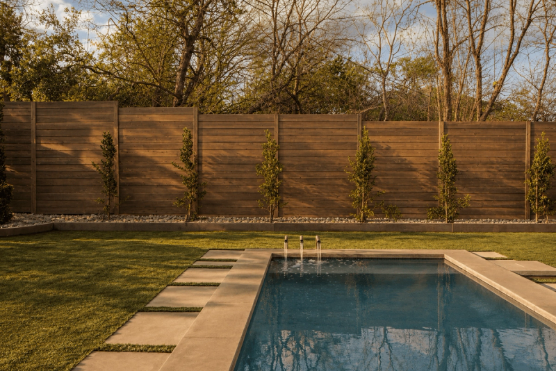 Golden Hour landscape with Lueders limestone pavers surrounding a gunite pool with fountain spouts, cedar fence, and lawn