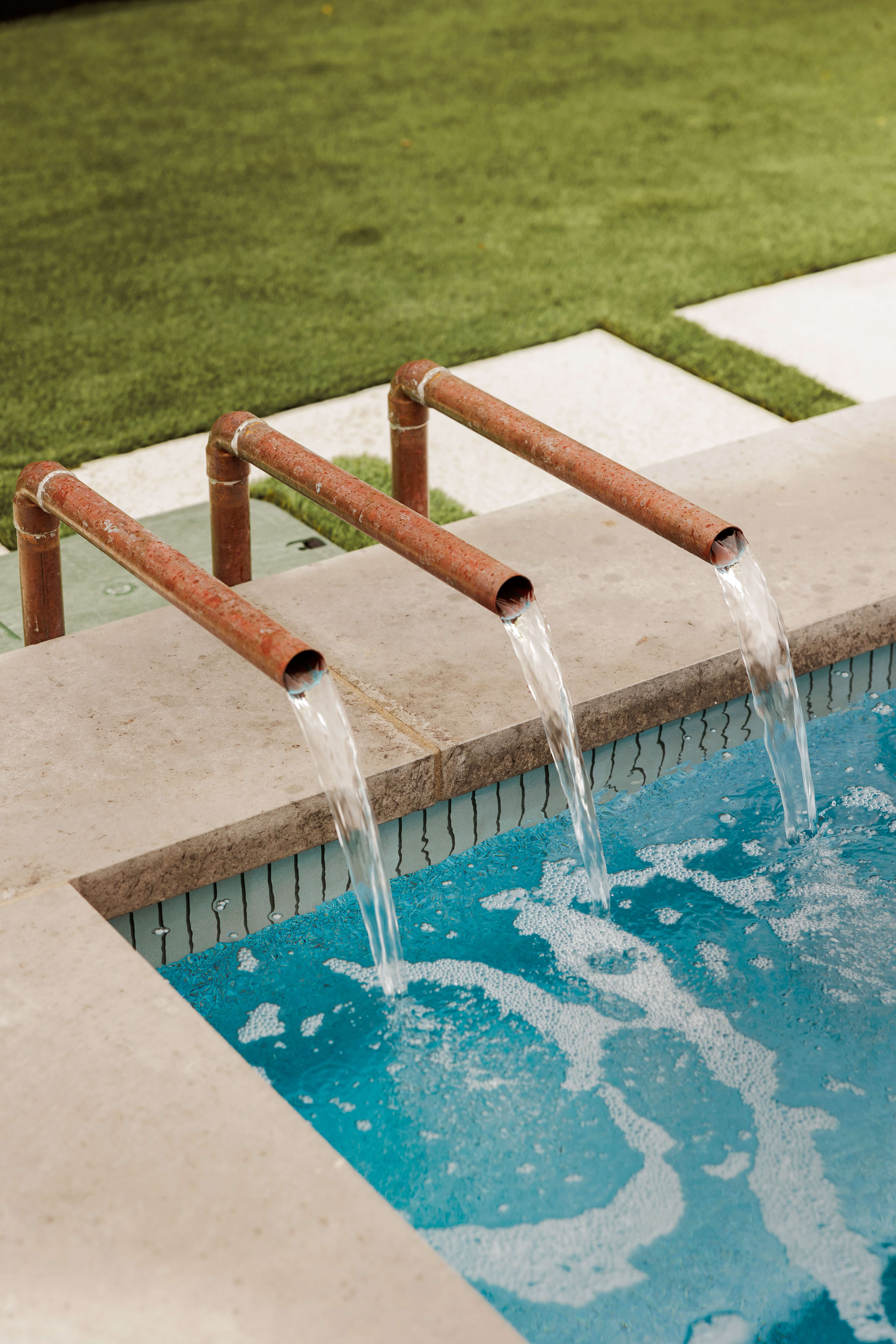 Golden Hour Pools Mini in Dallas, featuring copper scuppers pouring over dark tile and gunite plaster finish