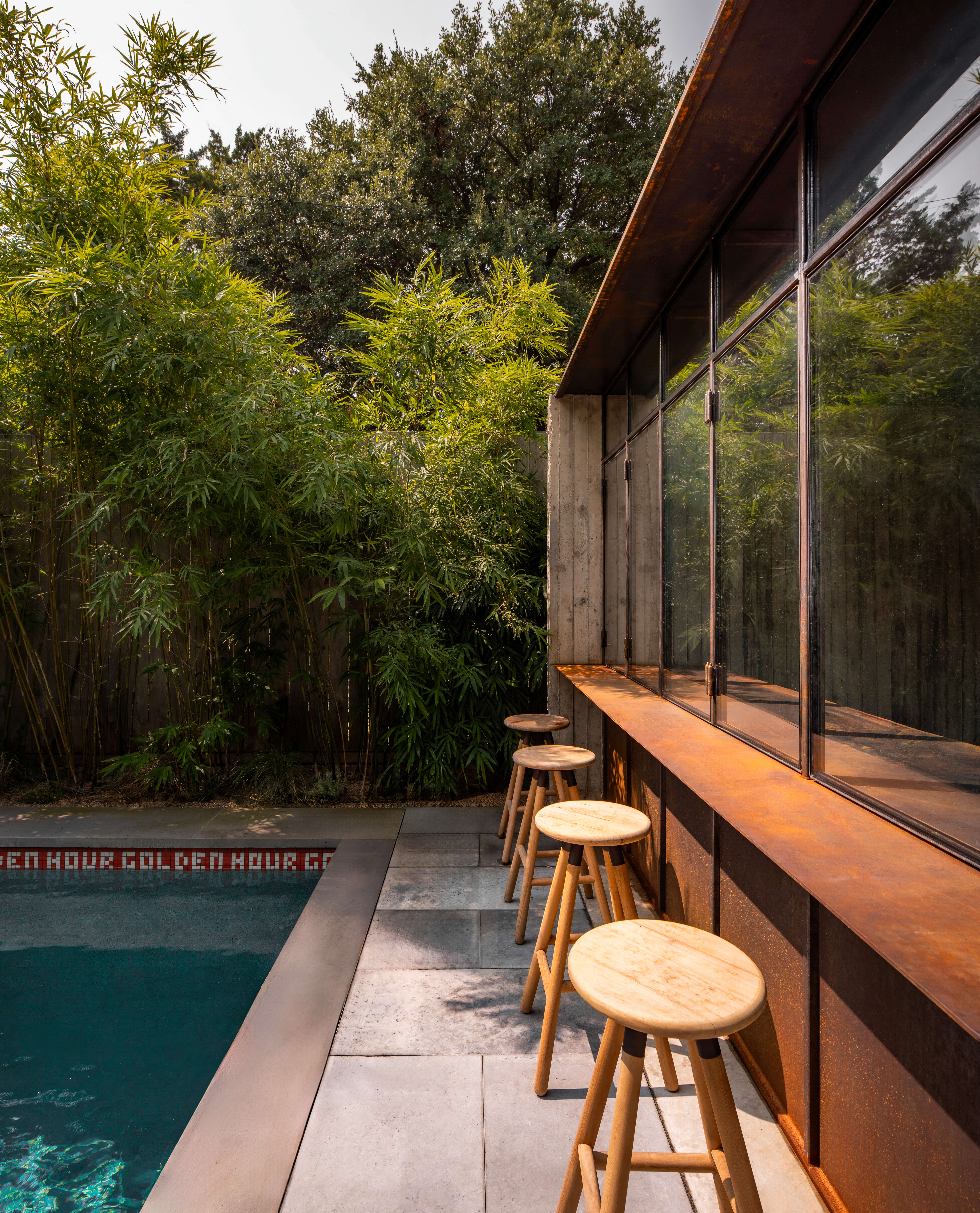 Wood bar stools along the glass-walled pool house bar beside the Dallas Grand pool