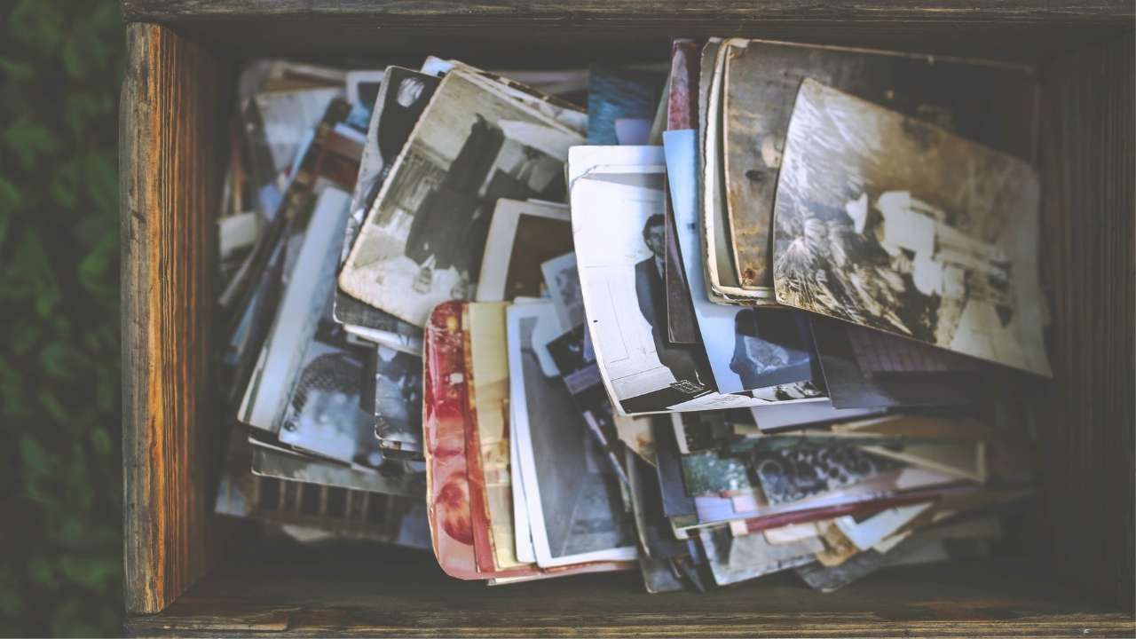 A top-down view of a wooden crate filled with an unorganized collection of vintage black-and-white and faded color printed photographs.