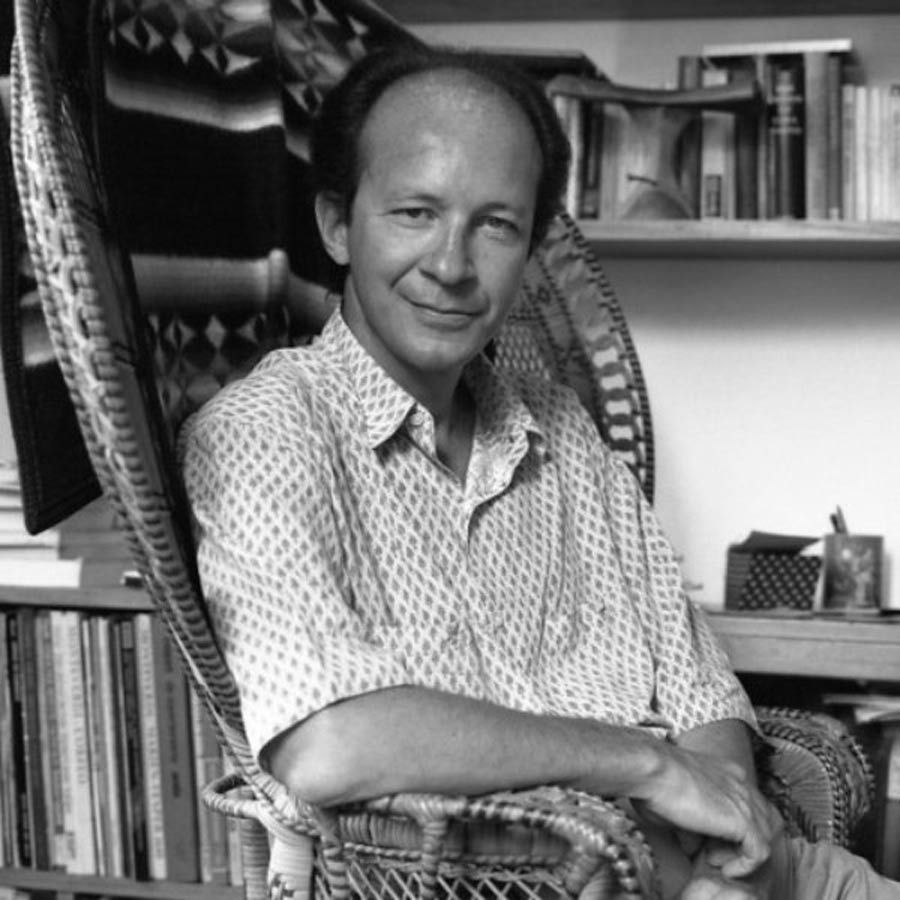 Image of political philosopher Giorgio Agamben sitting in his desk wearing a short-sleeved shirt.