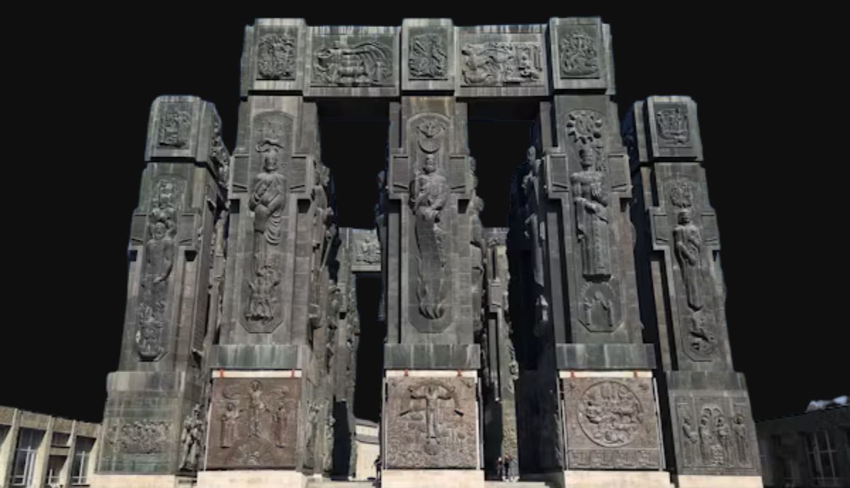 Large stone pillars of the Chronicle of Georgia monument covered in intricate historical and religious carvings.