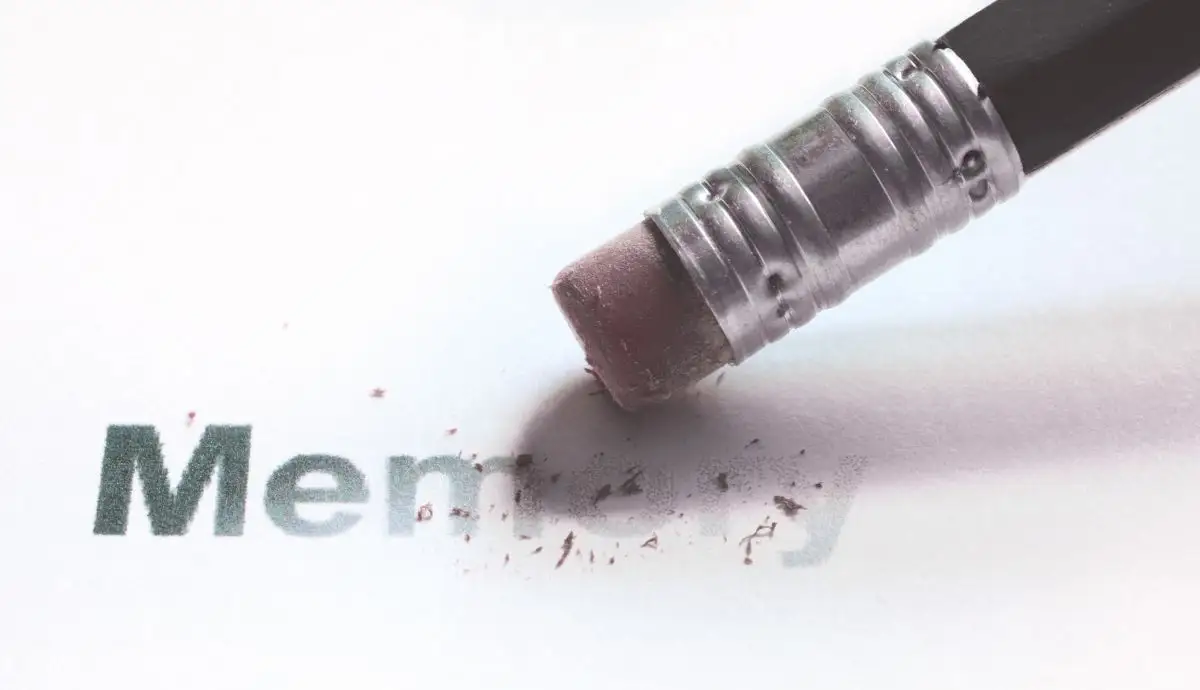 Close-up of a pencil eraser rubbing out the printed word "Memory" on white paper, leaving behind eraser shavings and faded letters.