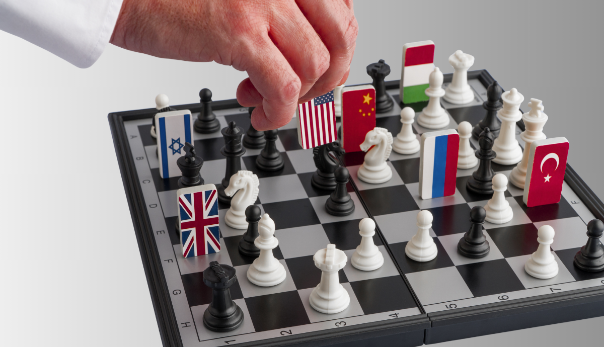 A hand moves a chess piece marked with the United States flag on a chessboard. Several other pieces on the board display national flags, including those of China, the United Kingdom, Russia, Israel, Turkey, and others.