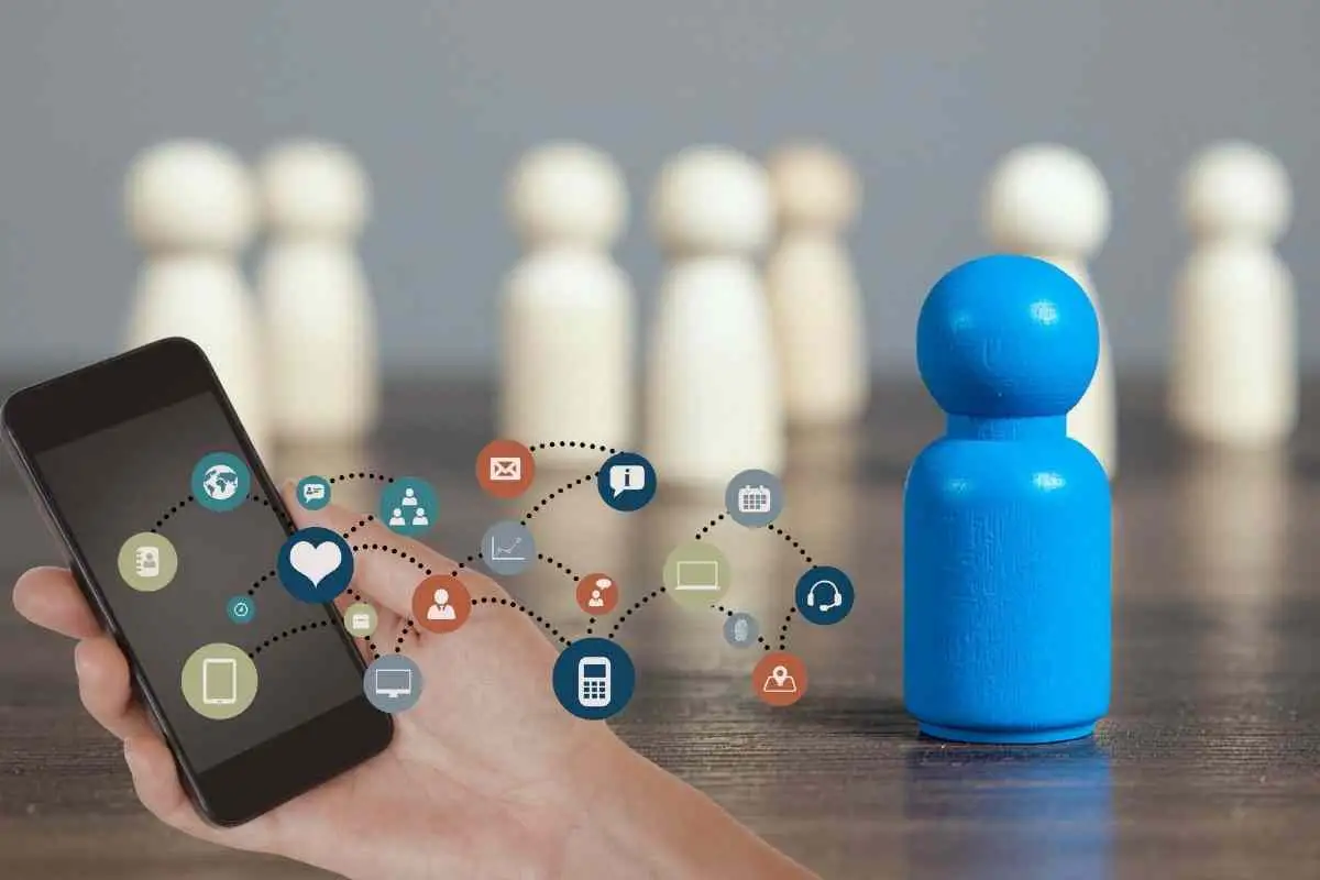 A conceptual image showing a hand holding a smartphone with floating social media icons next to wooden peg dolls, representing digital identity and connectivity in the age of algorithms.