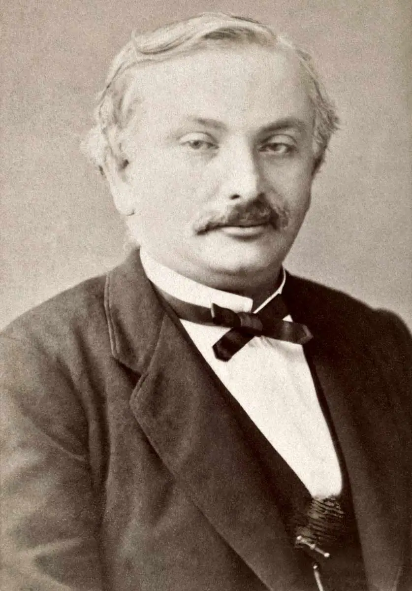 A sepia-toned portrait photograph of a man with a mustache, dressed in a dark suit jacket, vest, white collared shirt, and a dark bow tie.
