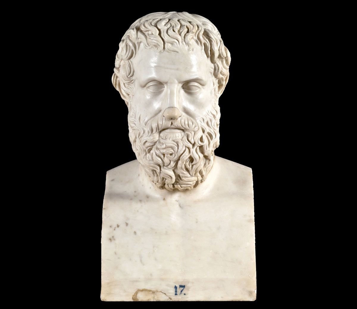 A front-facing white marble bust of Aeschylus, a bearded man with short, curly hair and a thick, wavy beard, sculpted in a classical style. The bust is shown from the chest up and is set against a solid black background. At the very bottom center of the marble base, there is a small blue number "17."