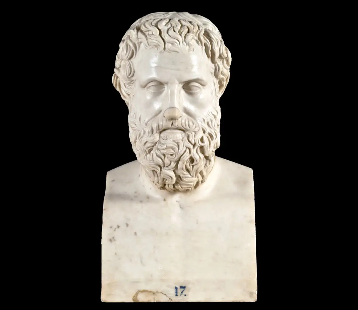A front-facing white marble bust of Aeschylus, a bearded man with short, curly hair and a thick, wavy beard, sculpted in a classical style. The bust is shown from the chest up and is set against a solid black background. At the very bottom center of the marble base, there is a small blue number "17."