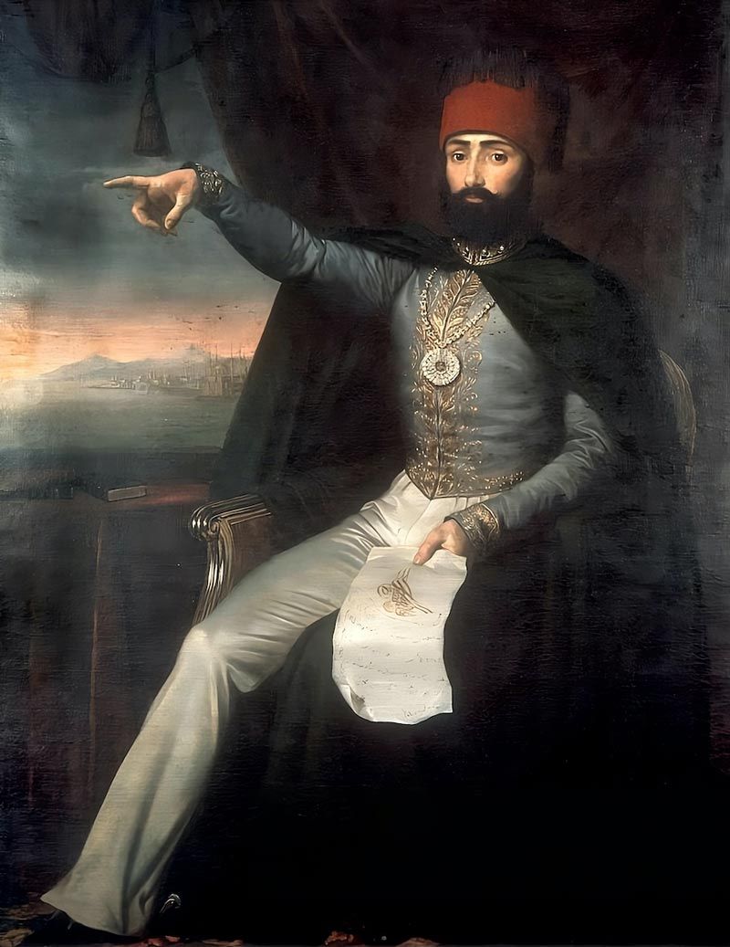 An oil painting of Ottoman Sultan Mahmud II seated on a chair, wearing a red fez and a blue military jacket with gold embroidery while pointing his right arm toward a distant harbor view.