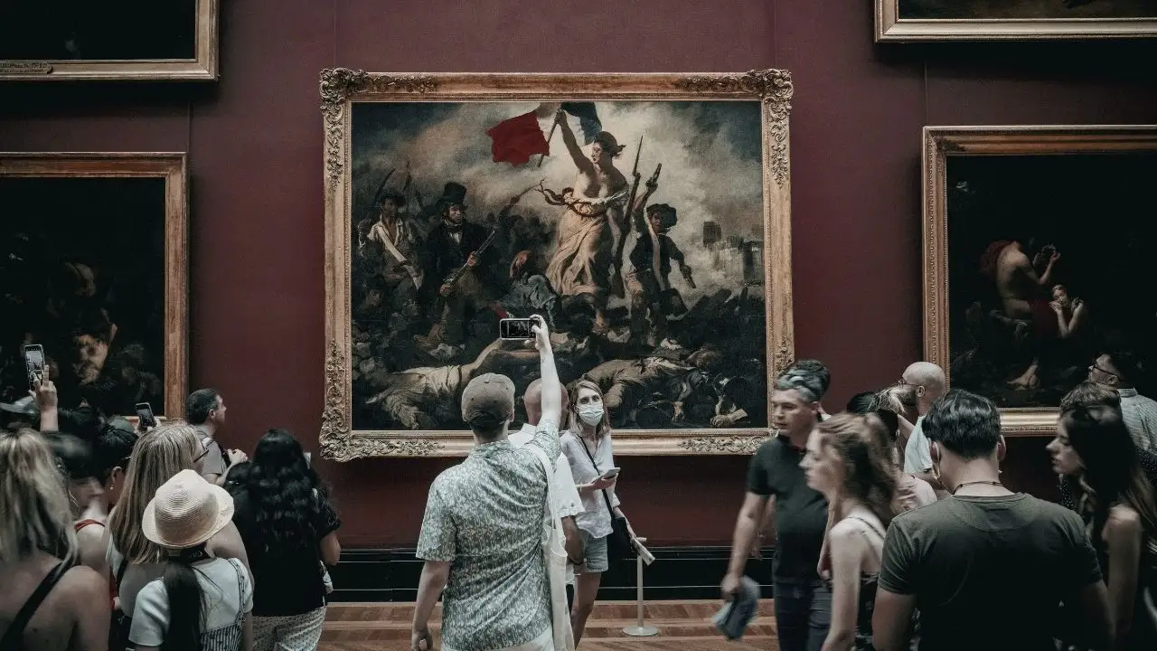 A dense crowd of museum visitors photographing and admiring Eugene Delacroix's painting Liberty Leading the People in the Louvre Museum