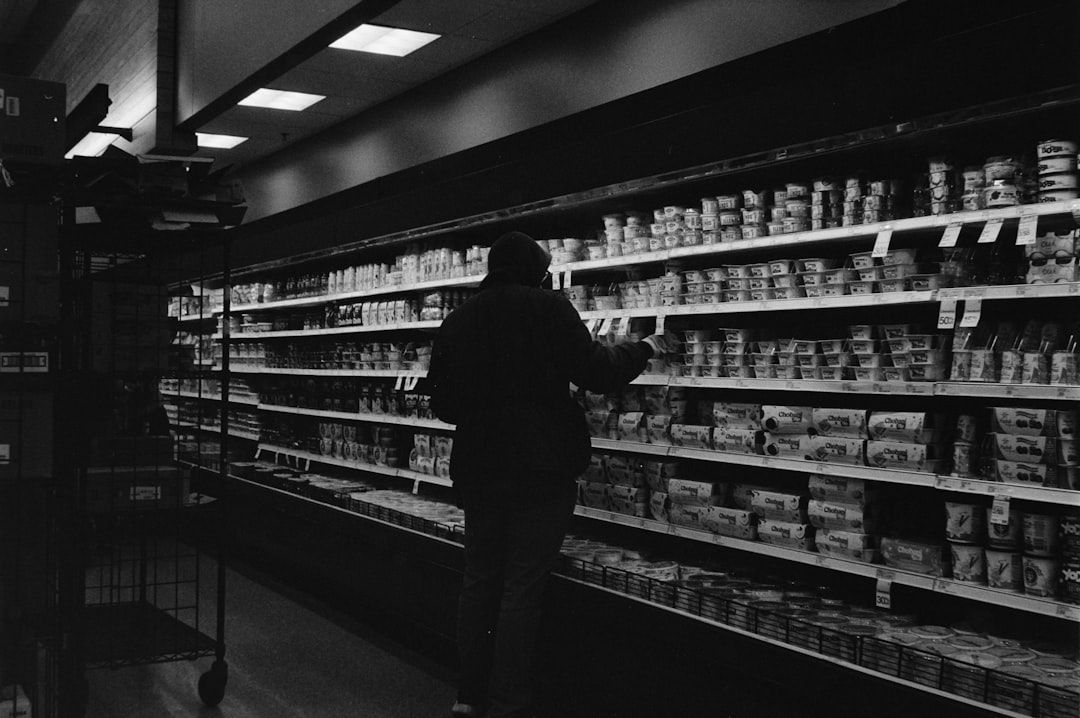 A shopper uses their smartphone to compare grocery prices while standing in a supermarket aisle.