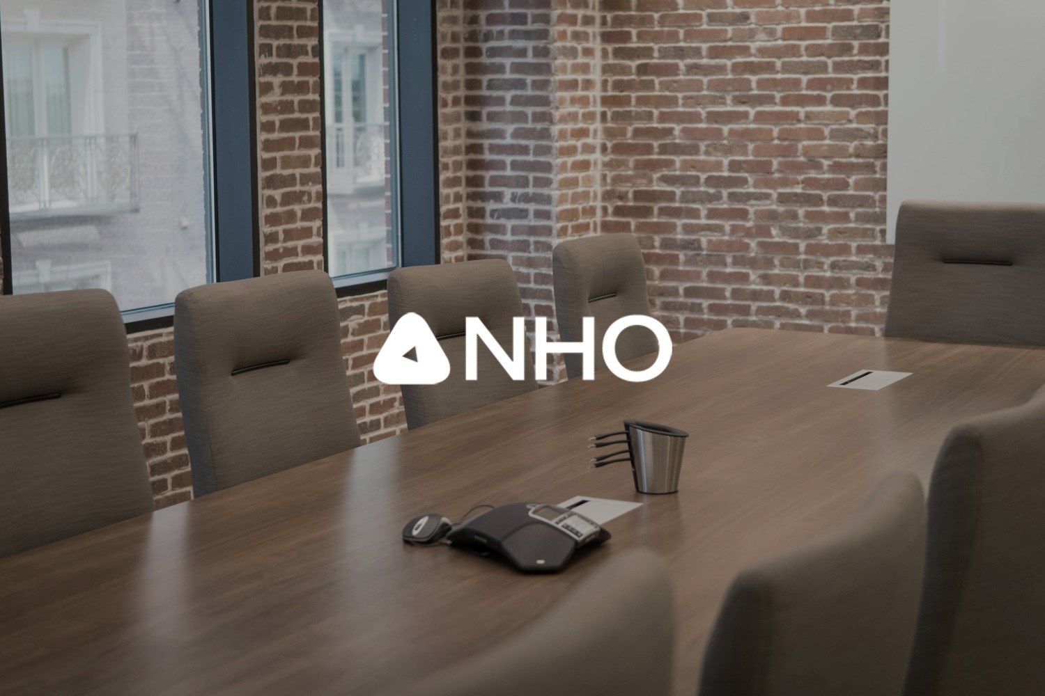 Et tomt møterom med et langt bord, kontorstoler og konferansetelefon. Med logoen til Næringslivets Hovedorganisasjon (NHO) lagt på.