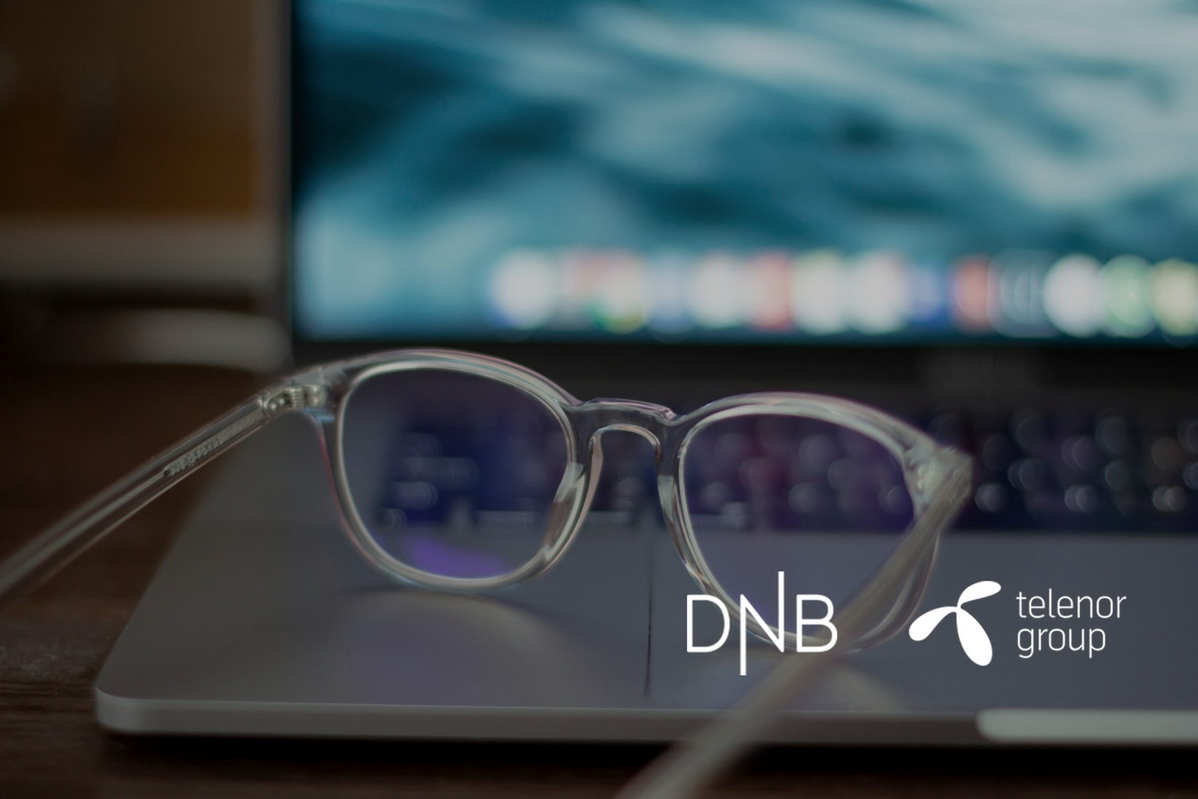 Et par briller ligger foran en åpen bærbar datamaskin. Med logoene til DNB og Telenor lagt på.