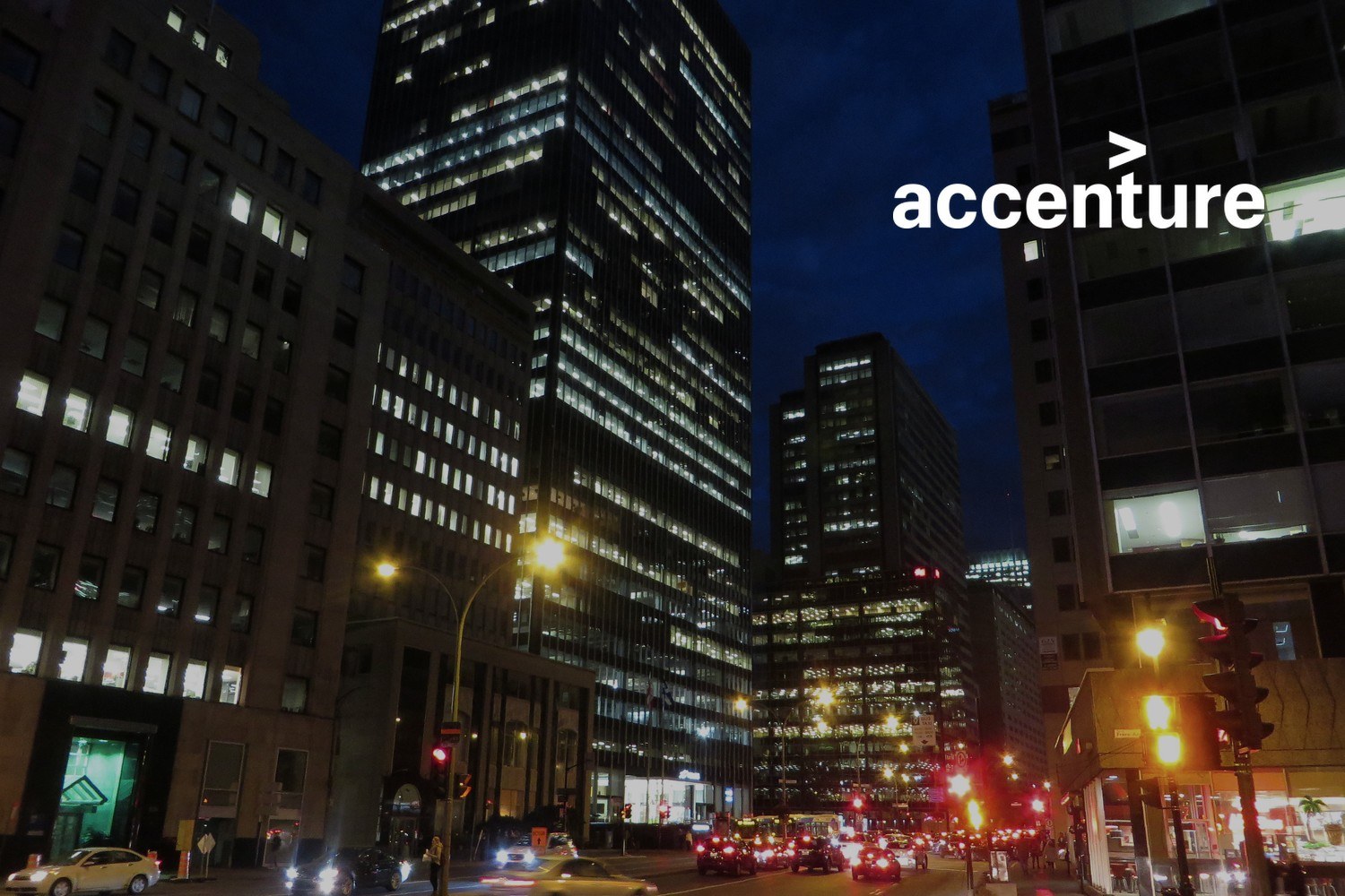 Kontorbygninger og trafikk i en bygate om kvelden. Med logoen til Accenture lagt på.