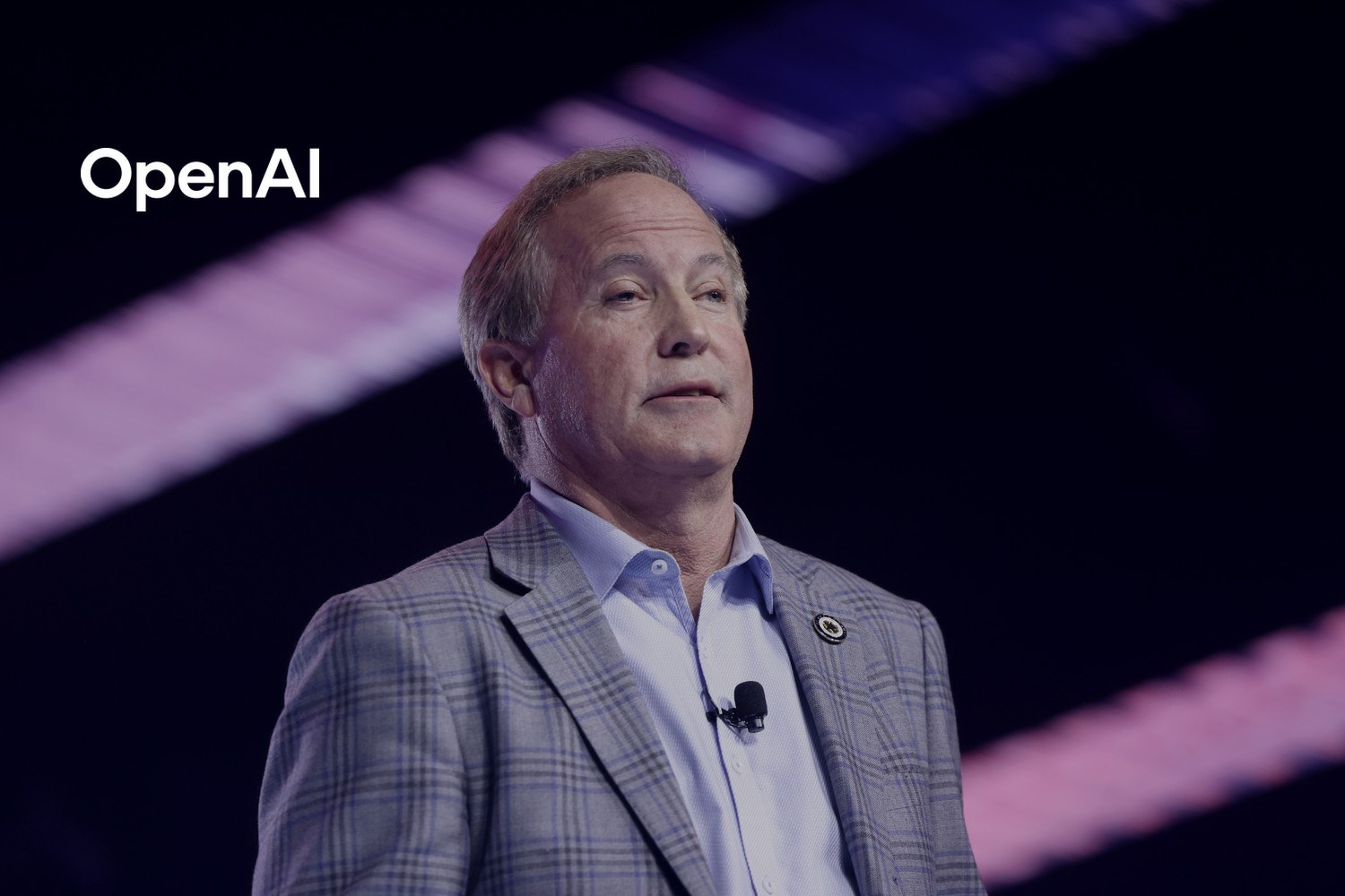 Texas' statsadvokat Ken Paxton taler på en scene under AmericaFest i Phoenix i Arizona. Med logoen til OpenAI lagt på.