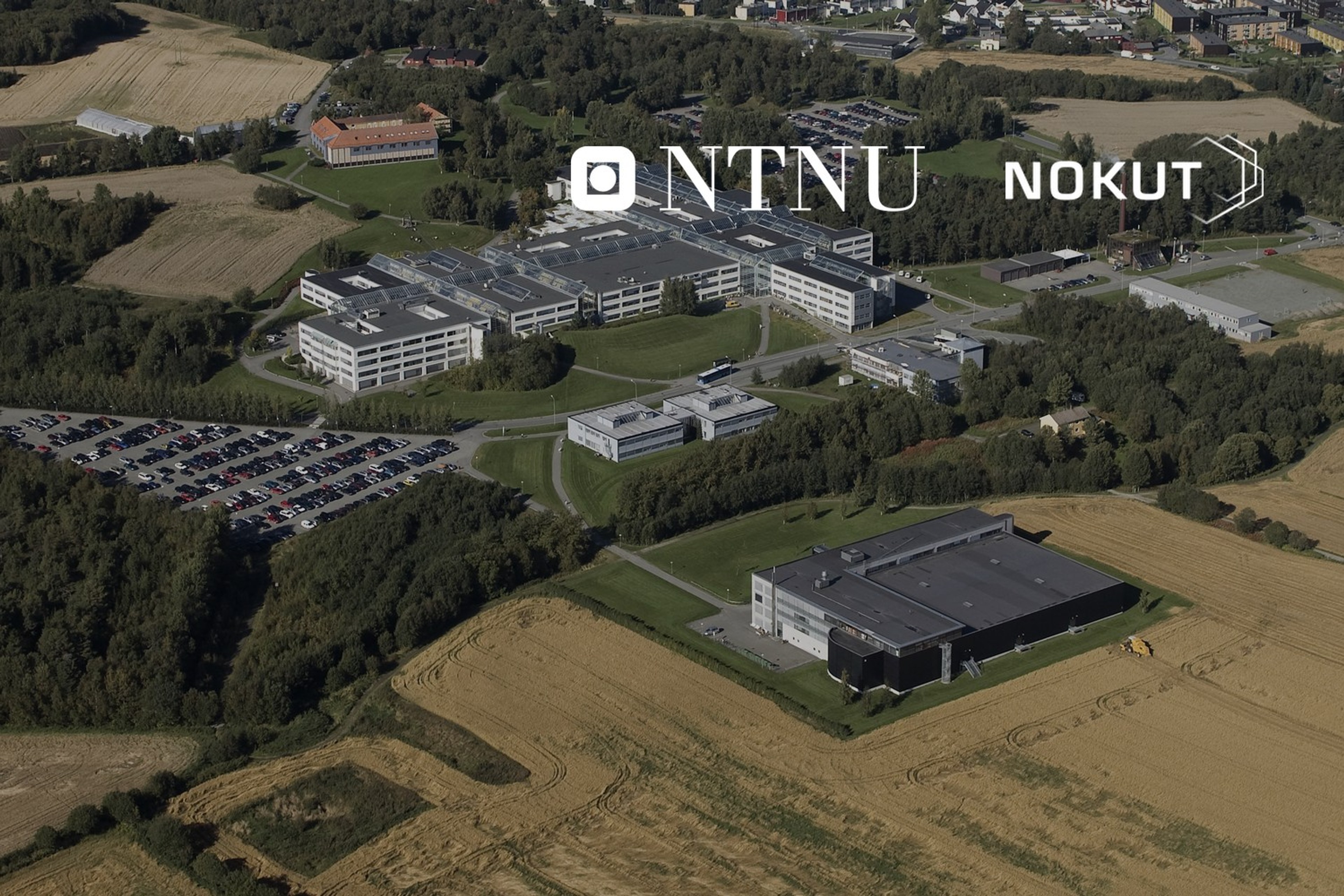 Flyfoto av NTNUs campus på Dragvoll med universitetsbygningene og deler av Trondheim i bakgrunnen. Med logoene til NTNU og Nokut lagt på.