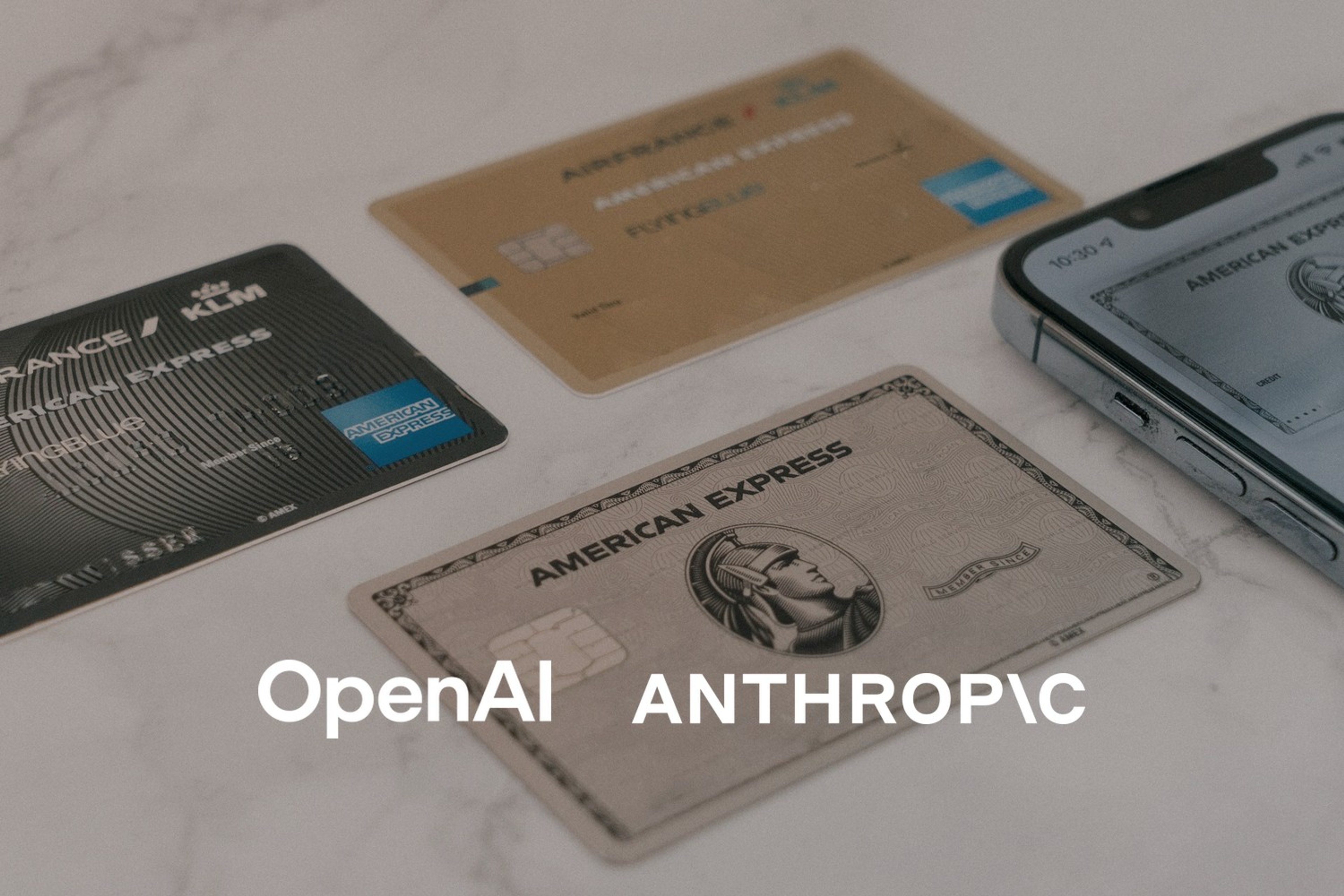 Flere betalingskort ligger ved siden av en smarttelefon på et lyst bord. Med logoene til OpenAI og Anthropic lagt på.