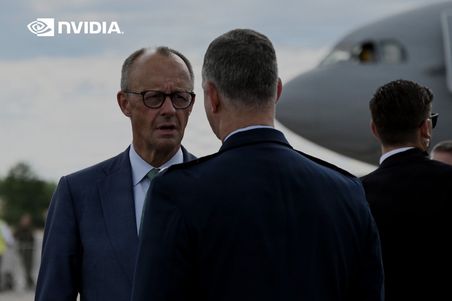 Tysklands forbundskansler Friedrich Merz snakker med general Alexus G. Grynkewich ved et amerikansk militærfly under flymessen ILA Berlin 2026. Med logoen til Nvidia lagt på.