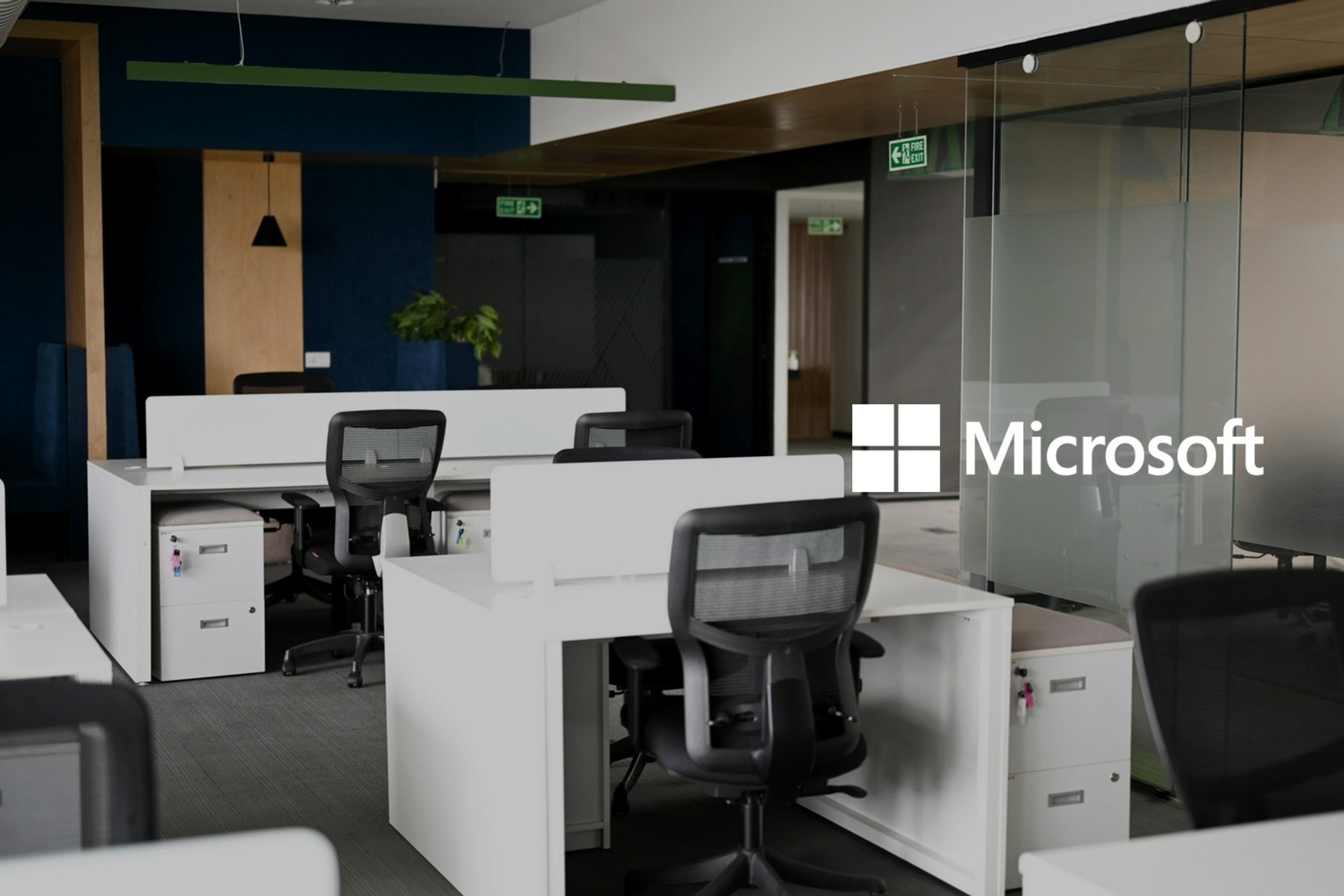 Et moderne kontorlandskap med hvite skrivebord og svarte kontorstoler. Med logoen til Microsoft lagt på.