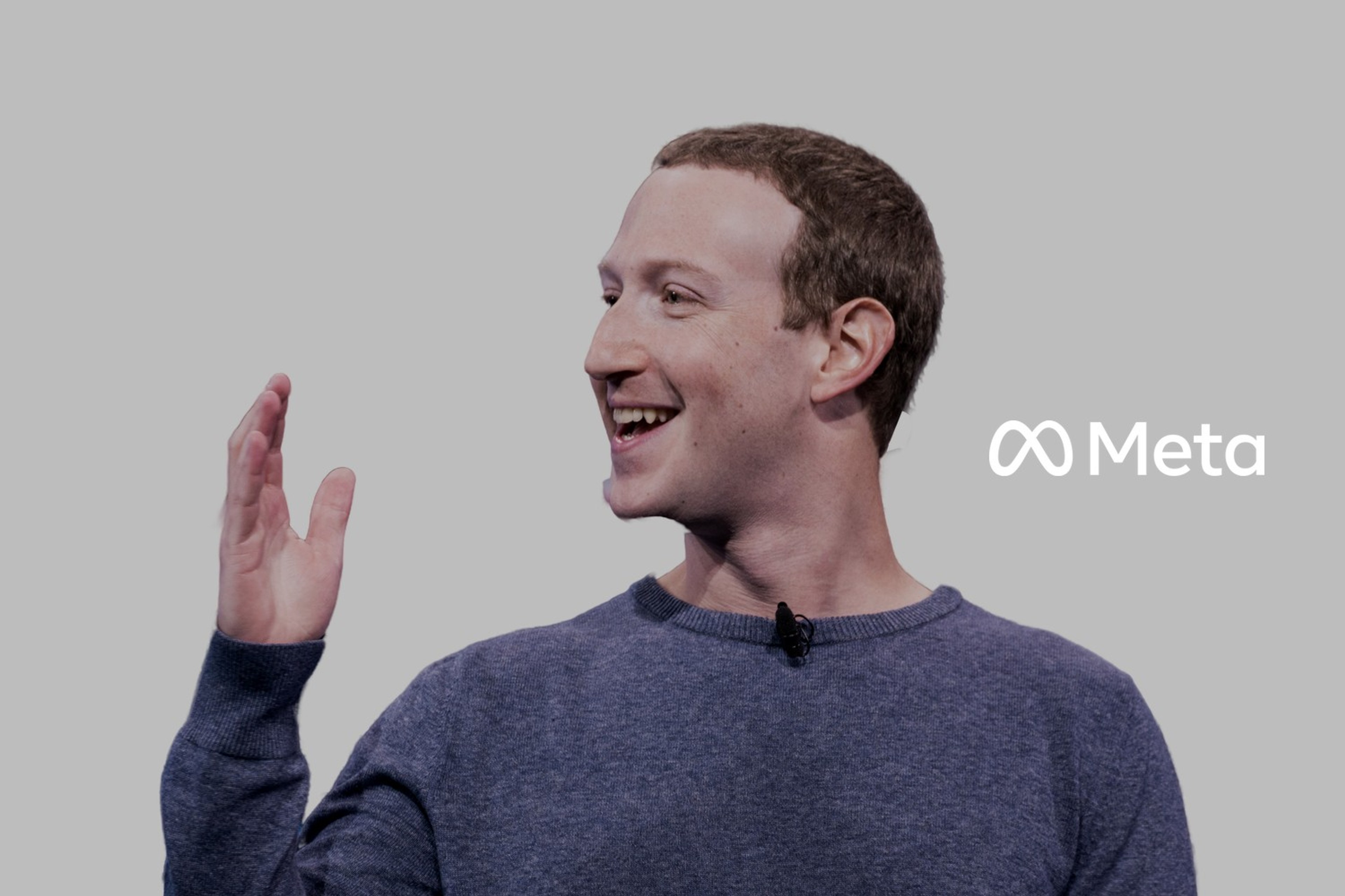 Mark Zuckerberg smiler og løfter hånden under en presentasjon på en scene. Med logoen til Meta lagt på.