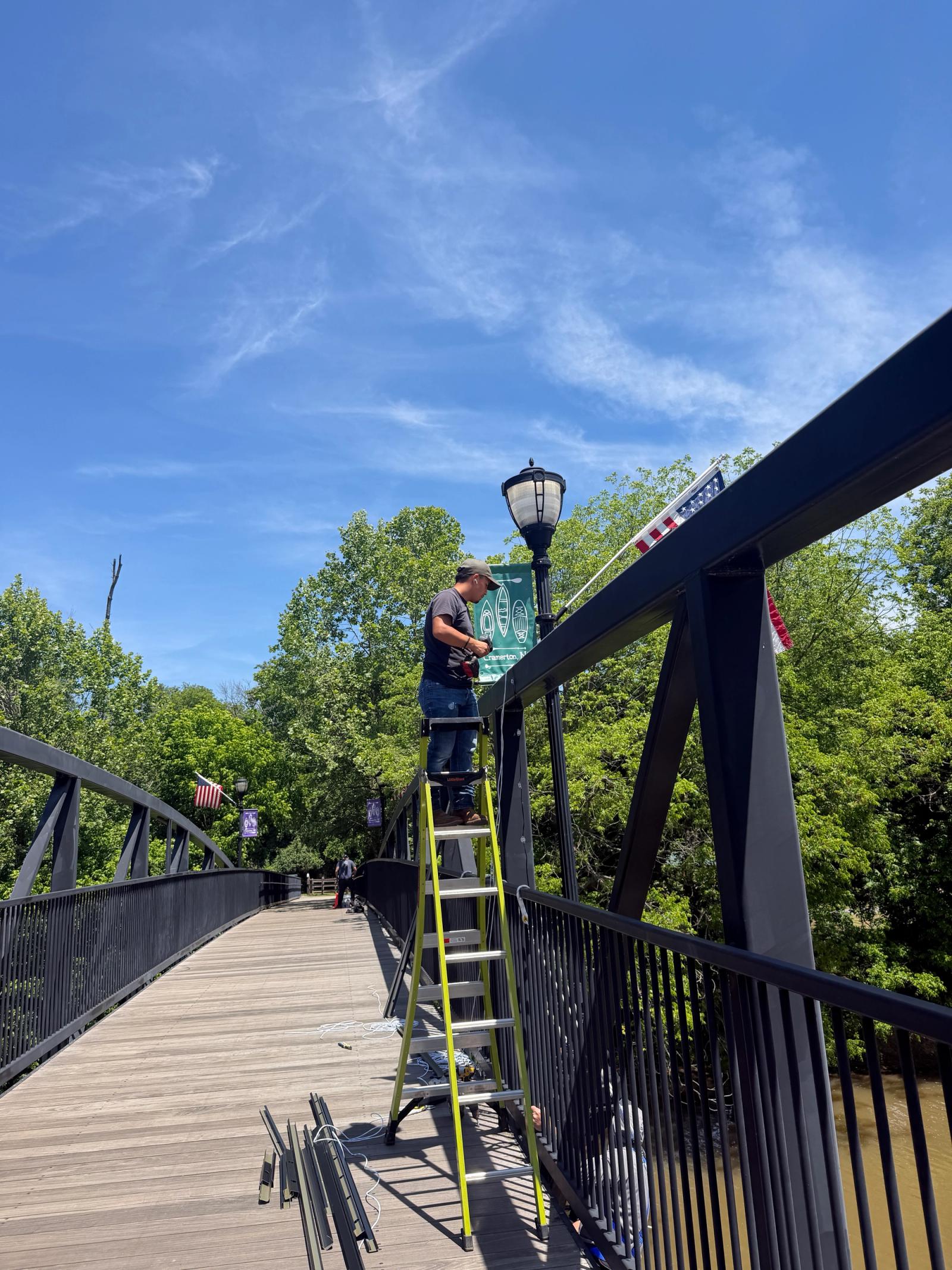 Installer on a ladder working near the bridge lamppost and town banners