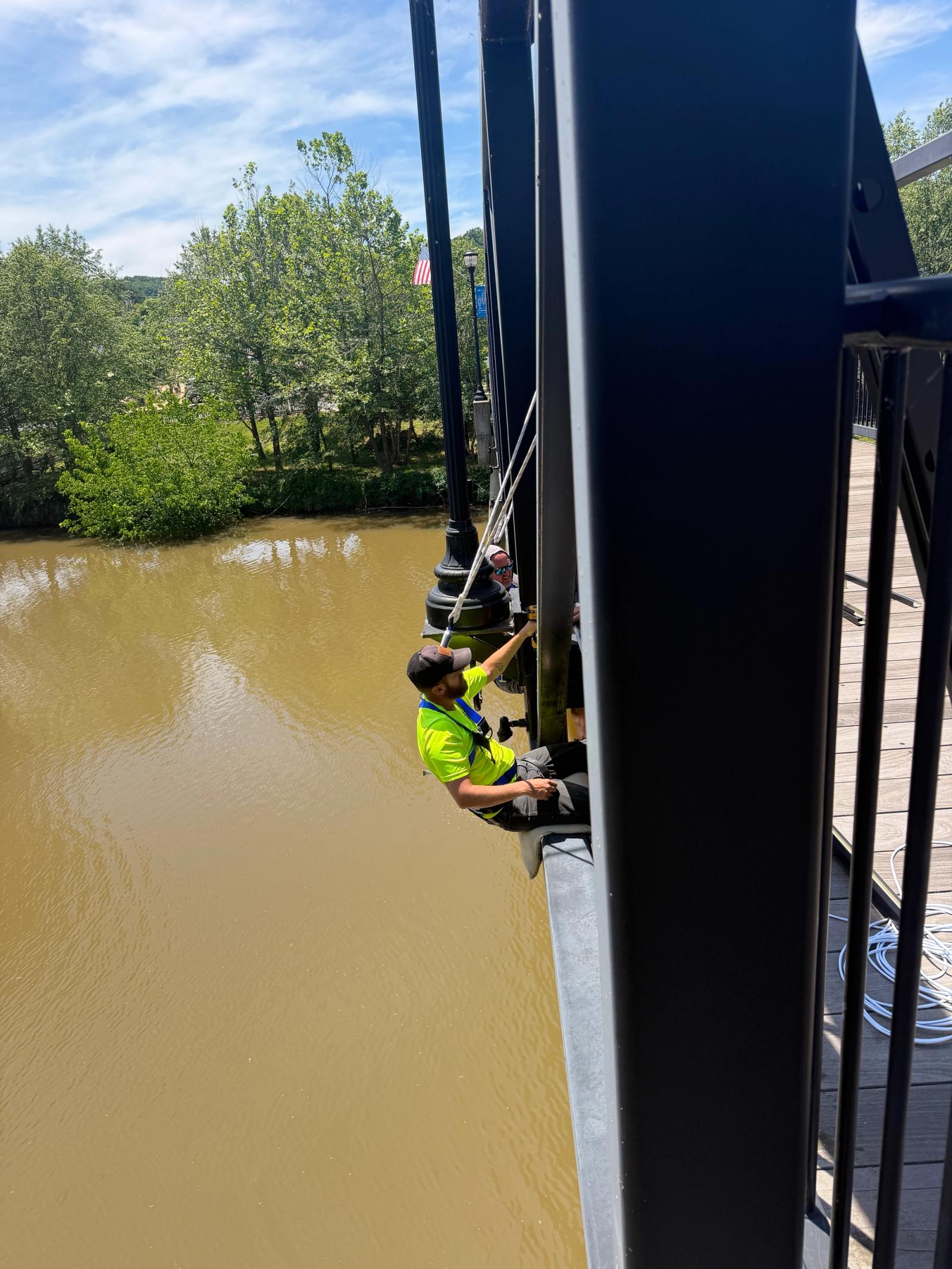 Installer in a hi-vis vest installing lighting out over the river