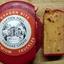 A wheel of Lupton Hall Dragon Bite spicy cheddar cheese in red wax, with a slice cut out on a wooden board showing the chili and jalapeño inside."