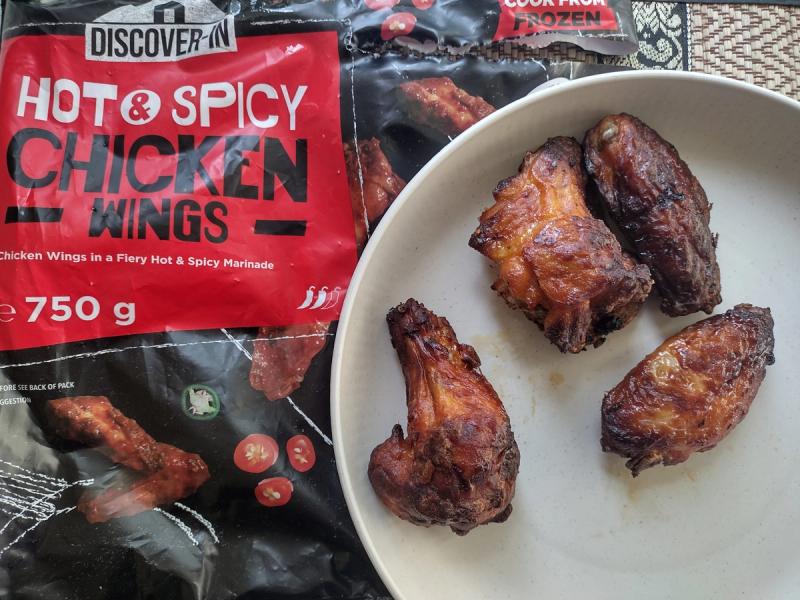 Crispy, cooked Discover-In Hot & Spicy Chicken Wings on a plate, with the black and red 750g packaging visible behind.