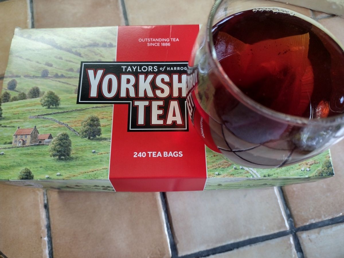 A red box of Taylors of Harrogate Yorkshire Tea sits next to a glass mug filled with the brewed black tea.