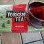 A red box of Taylors of Harrogate Yorkshire Tea sits next to a glass mug filled with the brewed black tea.