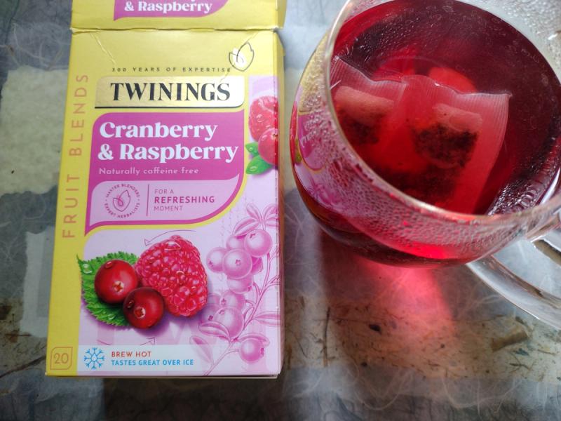 A box of Twinings Cranberry & Raspberry fruit tea next to a glass pitcher of the freshly brewed, vibrant red tea.