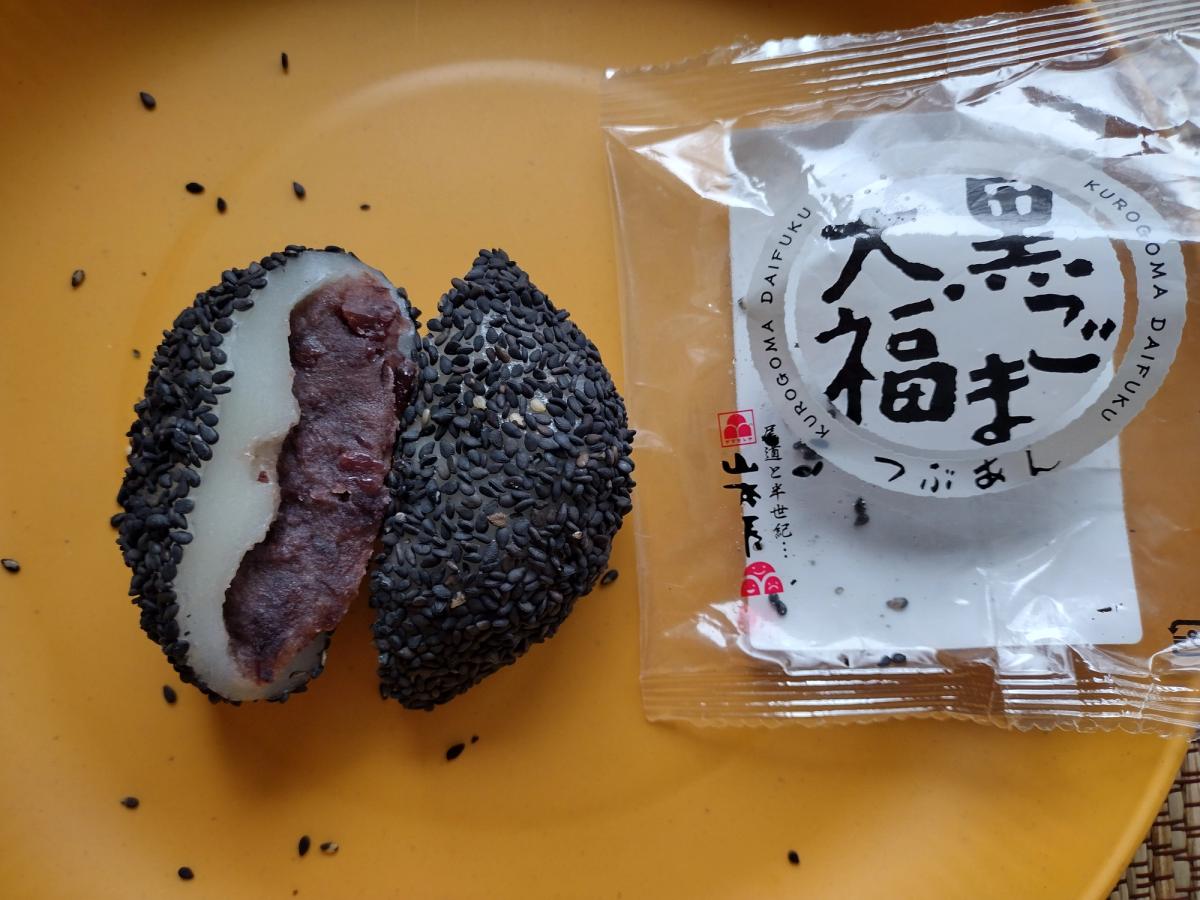  Cross section of a Yamamotoya Black Sesame Daifuku on a yellow plate showing the chunky red bean tsubu-an filling and thick black sesame seed coating, next to the open Japanese packaging.