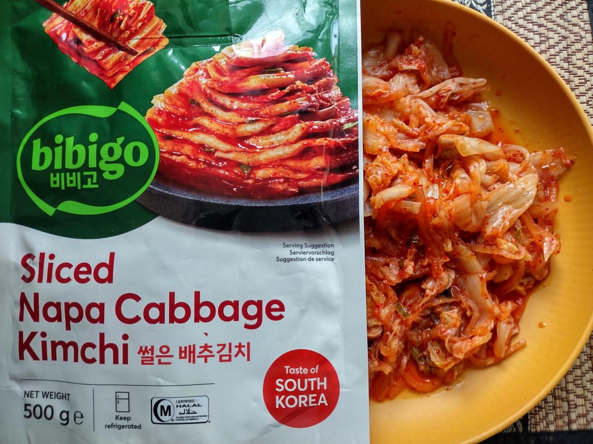 Jongga Traditional Korean Cut Cabbage Kimchi Mat Kimchi 500g package next to a white bowl serving of red spicy fermented cabbage and radish