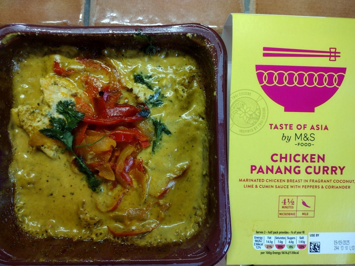 An overhead review photo of the M&S Taste of Asia Chicken Panang Curry. The prepared Thai curry is shown in its dish next to the yellow and pink product sleeve.