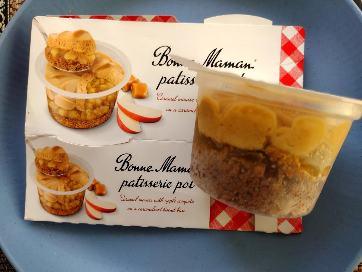 Bonne Maman Apple and Caramel Patisserie Pot packaging from Tesco next to a clear dessert cup showing layers of caramel mousse, apple compote, and a caramelised biscuit base on a blue plate.