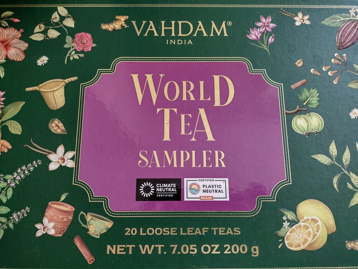 The green and purple Vahdam India "World Tea Sampler" box lid, decorated with illustrations of lemons, teacups, spices, flowers, and plants. Label shows "20 Loose Leaf Teas" with certifications for Climate Neutral and Plastic Neutral.