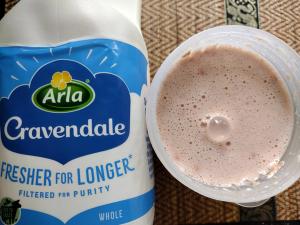 A top-down view of the Sneak Eats strawberry shake mixed with whole milk, showing its creamy and foamy texture next to a bottle of Arla Cravendale milk.