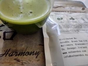 Shizuoka Organic Matcha in a clear cup after being whisked, showing a nice green and froth next to packaging.