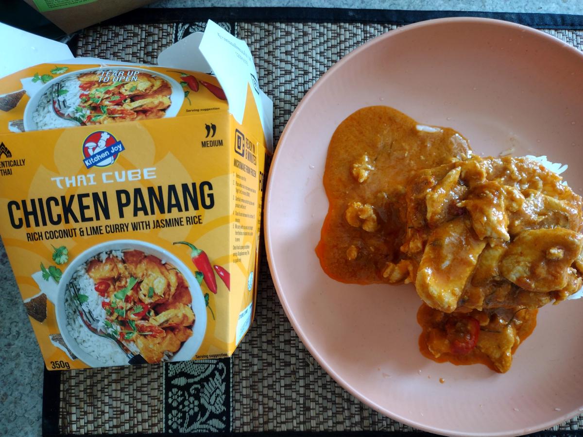 Review image of the Kitchen Joy Thai Cube Chicken Panang ready meal. The finished dish of chicken curry and rice sits on a plate next to the official product packaging, showing the branding and serving suggestion.