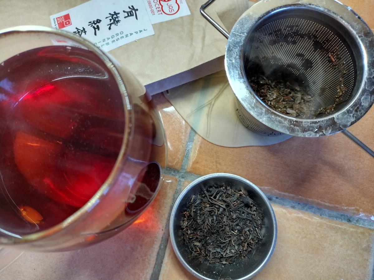Brewed Ocha & Co Organic Benifuki Black Tea in a glass mug showing ruby red colour, next to dry loose leaves and JAS organic packaging.
