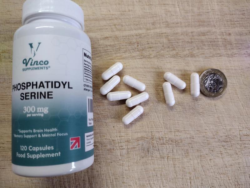 A bottle of Vinco Supplements Phosphatidylserine 300mg with its white capsules displayed next to a one pound coin on a wood surface.